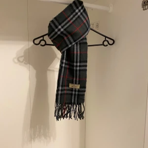 Burberry - Säljer nu denna Snygga halsduk från Burberry i färgen grå. Tillverkad i mjukt lammull med klassiskt fransad kant. Perfekt för att hålla dig varm och stilren under kyliga dagar. Hör av er vid funderingar☺️