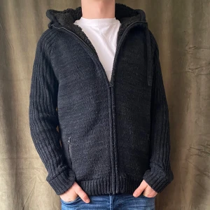 Fodrad Cardigan - Säljer en svart stickad fodrad cardigan jacka med huva och dragkedja. Jackan har en mysig fleecefodring och ribbade muddar. Perfekt för kyliga dagar! Den är lite nopprig men annars fint skick. Jag på bilden är 184 och väger ca 78kg! Vid minsta fråga eller fundering hör av er🤝