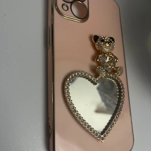 Rosa mobilskal med nalle och hjärtspegel - Snyggt rosa mobilskal dekorerat med en glittrig nalle och en hjärtformad spegel. Oanvänt och fräscht! 