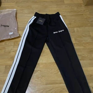 Svarta träningsbyxor från Palm Angels - Snygga svarta träningsbyxor från Palm Angels med vita sidoremsor och elastisk midja. . Kostar 1000kr.trapstar tracksuit kostar 1000kr den är storlek medium. Nike teck kostar 1600kr med byxor den är också storlek medium .Grå ralph lauren tröja kostar 1000kr den är storlek medium. Och den sista kostar 1200kr storlek medium kläderna är helt nya om ni vill ändra priset hör av er