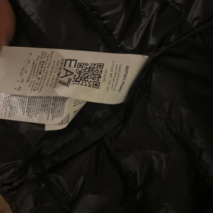 Svart dunväst från EA7 Emporio Armani - Snygg svart dunväst från EA7 Emporio Armani med dragkedja framtill. Perfekt för lager-på-lager under kyliga dagar. Diskret logga på bröstet ger en stilren look. Endast använd 2 ggr Köpte för 1600 men den passade inte så bra så bestämde mig för att sälja den 