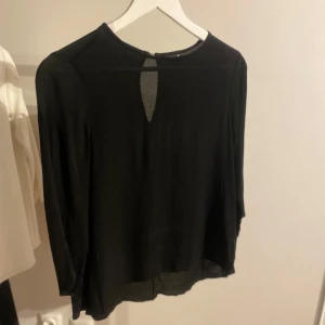 Svart blus från Gina Tricot - Snygg svart blus från Gina Tricot med långärmad design och en liten öppning bak i nacken. Perfekt för både vardag och festliga tillfällen.
