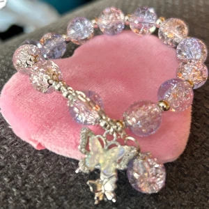 Elastiskt armband med fjärilsberlock! - Fint elastiskt armband med lila pärlor och en fjärilsberlock. Nytt!