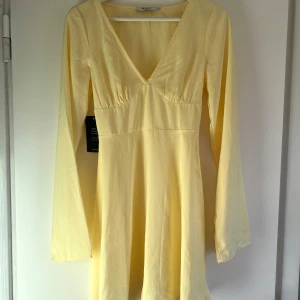 Gul klänning med v-ringning - Gul midi-klänning med v-ringning och långa ärmar från NA-KD. Klänningen har en knytning i ryggen för en fin passform. Perfekt för vår och sommar. Perfekt skick med prislappen kvar, säljs dock pga för liten. Storlek 38 men skulle säga att den är mer som 36. Skriv gärna vid frågor🤗