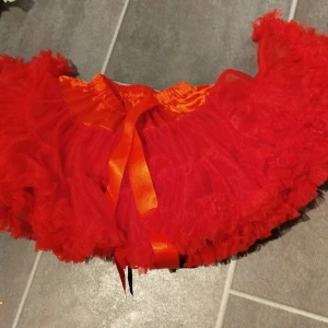 Röd volangkjol med rosett (för barn) - Säljer en härlig röd volangkjol med en fin rosett i midjan. Kjolen har flera lager av volanger som ger en fluffig och lekfull look. Perfekt för att sätta färg på din outfit!