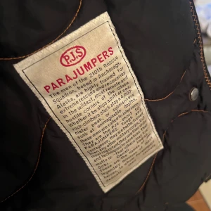 Svart parkajacka från Parajumpers - Säljer en svart parkajacka från Parajumpers med pälsdetaljer på huvan och en gul rem. Jackan har flera fickor och en broderad patch på ärmen. Perfekt för kalla dagar med sin quiltade insida och robusta design.