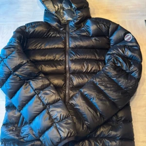 Svart pufferjacka från Colmar - Säljer en snygg svart pufferjacka från Colmar i ny skick. Jackan har en dragkedja framtill och en mysig huva för extra värme. Perfekt för kalla vinterdagar och höstpromenader. Den är både stilren och funktionell, vilket gör den till ett måste i garderoben!