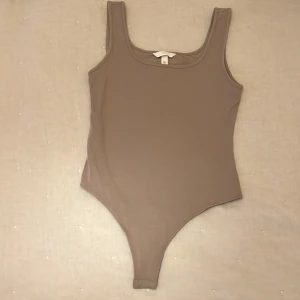 Beige ärmlös bodysuit från H&M - Snygg beige bodysuit i ett mjukt och stretchigt material. Perfekt för lager-på-lager eller att bära som den är. Den är ärmlös med en rund halsringning, vilket gör den superbekväm och lätt att matcha med olika outfits. Ett måste i garderoben för alla säsonger! Aldrig använd!