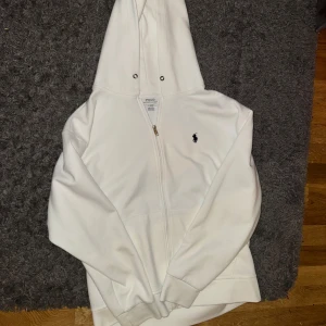Vit zip från Polo Ralph Lauren - Säljer en stilren vit hoodie från Polo Ralph Lauren. Den har en dragkedja framtill och en klassisk logga på bröstet. Perfekt för både vardag och chill. Den är i mycket bra skick och supermjuk. Man får med snören. Storlek L men passar M väldigt bra 