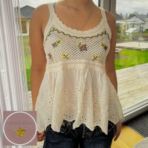 Vit UNIK broderad linneblus - Superfint UNIKT vit linneblus med broderade blommor i grönt och gult. Den har en luftig passform med spetsdetaljer och är ärmlös. Perfekt för sommardagar eller en avslappnad vårlook. Passar bra till jeans eller kjol för en bohemisk stil.