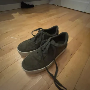 Gröna sneakers i mocka - Säljer ett par gröna sneakers i mocka med snörning och vit sula. De är i storlek dam 38 och i bra skick. Perfekta för vardagsbruk och ger en stilren look.