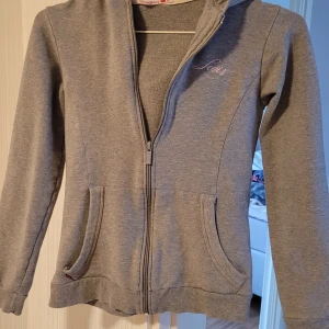 Grå hoodie från Levi's - Säljer en snygg grå hoodie från Levi's i mycket bra skick. Den har en dragkedja framtill och två praktiska fickor. På baksidan finns ett coolt tryck med texten 'Levi's 53'. Perfekt för höst och vår!