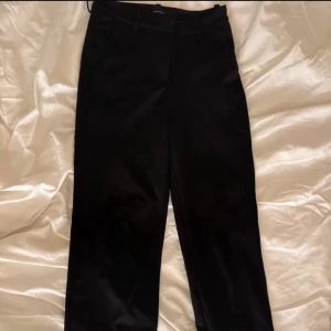 Svarta kostymbyxor från Vero Moda - Snygga svarta kostymbyxor från Vero Moda i ett klassiskt snitt. De har en dragkedja fram och är perfekta för både jobb och fest. Byxorna är i ett mjukt och bekvämt material som ger en elegant look. Passar perfekt till en skjorta eller blus för en stilren outfit.