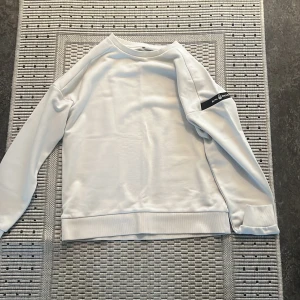 Vit sweatshirt från sail racing - Säljer en stilren vit sweatshirt från sail racingDen har långa ärmar och en liten logga på ärmen. Perfekt för en avslappnad look eller som lager under jackan. Passar både till vardags och träning.