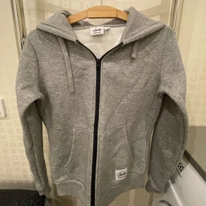 Grå hoodie från Andy by Frank Dandy - Säljer en snygg och bekväm grå hoodie från Andy by Frank Dandy. Den har en dragkedja framtill och praktiska fickor. Perfekt för en avslappnad stil och passar till alla tillfällen. Huvan har dragsko för justering. Perfekt för höst och vår!