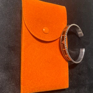 Orange och silver armband med mönster - Snyggt armband i svart och silver med ett coolt. Kommer med en orange förvaringspåse. Passar både till vardags och fest.