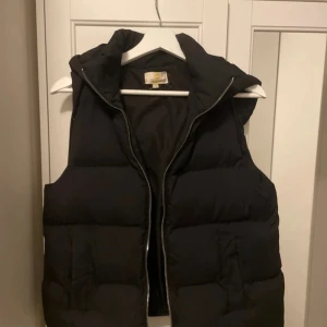 Svart dunväst från Chelsea  - Säljer en svart dunväst från Chelsea i bra skick. Västen har en dragkedja framtill och är perfekt för höst och vinter. Den är vadderad och håller dig varm under kyliga dagar. Passar bra till både vardag och utomhusaktiviteter.