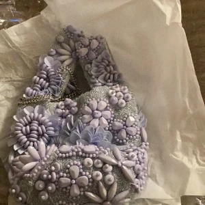 Zara Ljuslila pärlbroderad handväska - Säljer en superfin ljuslila handväska med massor av pärlor och blommiga detaljer. Väskan har en kedja som axelrem och är perfekt för festliga tillfällen. Den är både unik och iögonfallande, perfekt för att ge din outfit det där lilla extra! 💜köptes för 600kr 