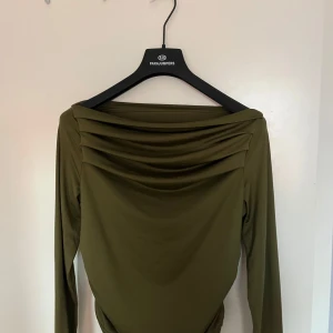 Olivgrön långärmad topp - Snygg olivgrön blus i ett mjukt och stretchigt material. Den har långa ärmar och en draperad detalj vid halsen som ger en elegant touch. Perfekt för höst och vår, både till vardags och festligare tillfällen.