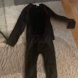 Svart underställ med röda detaljer - Säljer ett svart underställ från Craft i mycket bra skick. Perfekt för kalla dagar med sina långa ärmar och bekväma passform. Röda detaljer längs ärmarna ger en sportig look. Passar utmärkt för vinteraktiviteter eller som baslager under skidkläder.