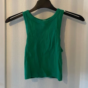 Grön ribbad linnetopp - Snygg grön ribbad linnetopp i ett mjukt och stretchigt material. Perfekt för sommardagar eller som ett lager under en jacka. Toppen är ärmlös och har en enkel design som gör den lätt att matcha med olika outfits.