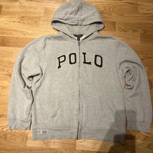 Grå zip hoodie från Ralph Lauren - Säljer en grå zip hoodie från Ralph Lauren i storlek L/XL. Den har en dragkedja framtill och en stor POLO-logga i svart på bröstet. Perfekt för en avslappnad stil och passar perfekt till vintern. Den är i mycket bra skick och superbekväm!