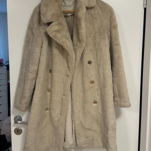 Beige faux fur kappa från Forever New - Säljer en supermysig varm beige fur från Forever New. Jackan har långa ärmar och silver knappar framtill🥰