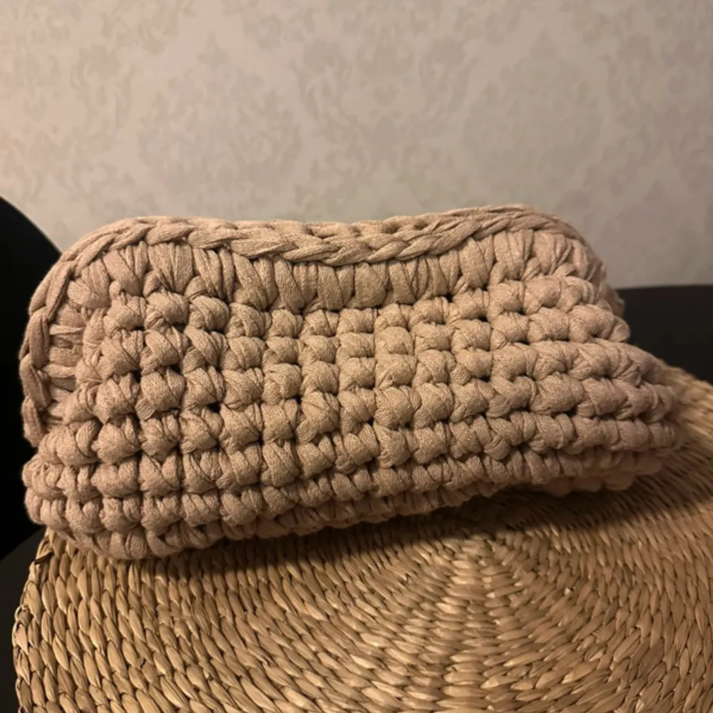 Säljer en superfin beige stickad handväska. Den är handgjord med ett grovt virkad mönster som ger en mysig och unik känsla. Perfekt för att bära med sig småsaker till vardags eller som en söt accessoar till en avslappnad outfit. 👜✨. Väskor.