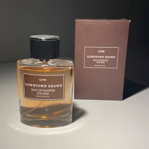 Downtown Brown Eau de Parfum för män - Säljer en elegant Downtown Brown Eau de Parfum från LCW. Flaskan är stilren och rektangulär med en svart kork och rymmer 100 ml. Doften är perfekt för den moderna mannen som vill ha en sofistikerad och maskulin touch. Kommer i en snygg brun förpackning. Perfekt för både vardag och speciella tillfällen.