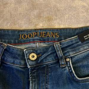 Säljer ett par snygga blå jeans från Joop! i mycket bra skick. De har en klassisk femficksdesign och en knappgylf. Perfekta för både vardag och fest. Passformen är normal och de är tillverkade i ett slitstarkt denimtyg.