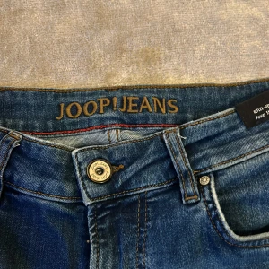 Blå jeans från Joop! - Säljer ett par snygga blå jeans från Joop! i mycket bra skick. De har en klassisk femficksdesign och en knappgylf. Perfekta för både vardag och fest. Passformen är normal och de är tillverkade i ett slitstarkt denimtyg.