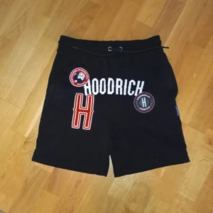 Svarta shorts från Hoodrich - Säljer ett par svarta shorts från Hoodrich i nyskick. De har coola tryck och broderade märken på framsidan. Shortsen har en elastisk midja med dragsko för bästa passform. Perfekta för en skön på stil i sommaren!!