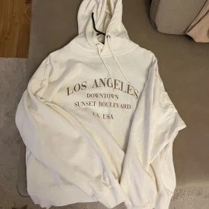 Vit hoodie  - En vit hoodie med tryck på framsidan. Huvan är fodrad med samma tyg som resten av tröjan.