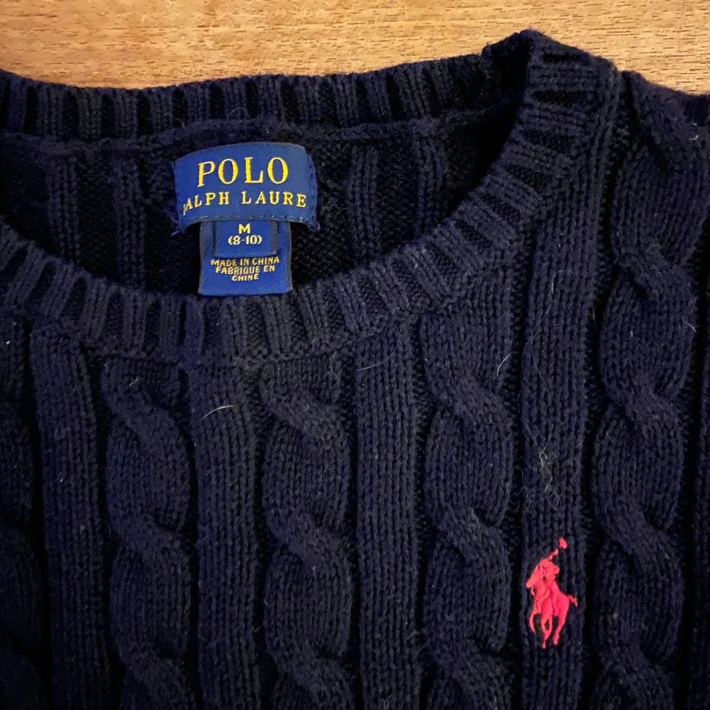 Säljer en snygg svart stickad tröja från Polo Ralph Lauren. Den har ett klassiskt flätmönster och den ikoniska röda loggan på bröstet. Perfekt för kyliga dagar och ger en stilren look. Passar både till vardags och lite finare tillfällen. Obs den är en barntröja 8-10 år. . Tröjor & Koftor.