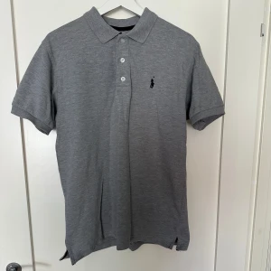 Grå pikétröja från Ralph Lauren - Säljer en stilren grå pikétröja från Ralph Lauren. Den har en klassisk krage och tre knappar framtill. Tröjan är dekorerad med det ikoniska broderade logotypen på bröstet. Perfekt för både vardag och lite finare tillfällen! Skriv för viktig info 9/10 en replika