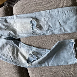 Ljusa jeans med slitningar från Gina Tricot - Säljer ett par ljusa jeans från Gina Tricot, storlek 38. De har coola slitningar på knäna som ger en avslappnad och trendig look. Perfekta för en casual outfit! Tillverkade i mer hållbar bomull.