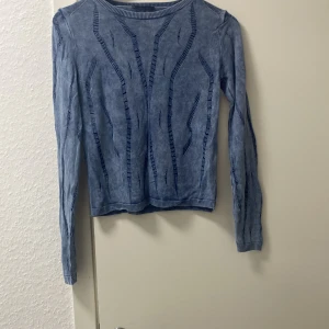 Blå stickad tröja från Avrile - Säljer en snygg blå stickad tröja från Avrile. Den har ett unikt mönster med vertikala linjer och är perfekt för både höst och vinter. Tröjan är långärmad och har ribbade kanter vid halsen och ärmsluten. Supermysig och stilren!