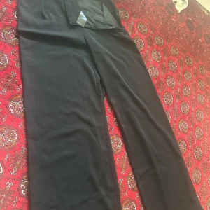 Svarta byxor från NA-KD - Säljer ett par stilrena svarta byxor från NA-KD. De är högmidjade och har en klassisk rak passform. Perfekta för både vardag och fest! 🖤De är uppsydda jag är 160 med dem är fortfarande för långa på mig.
