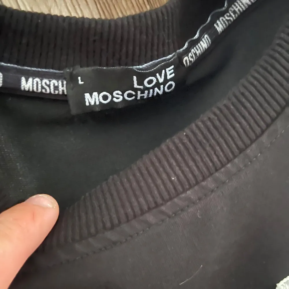 Säljer en svart tröja från Love Moschino med ett gulligt nallemotiv på framsidan. Tröjan har långa ärmar och är perfekt för en avslappnad stil. Den är i bra skick och redo för nya äventyr! 🐻🖤. Tröjor & Koftor.