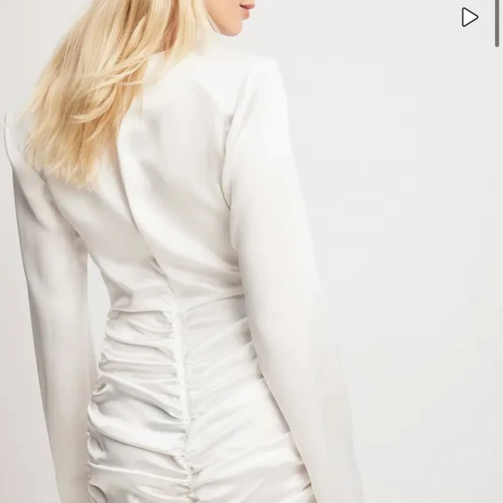 Säljer en elegant vit klänning i satin med långa ärmar. Klänningen har en tight passform och snygga rynkdetaljer längs sidorna som ger en smickrande siluett. Perfekt för festliga tillfällen eller en stilren look.. Klänningar.