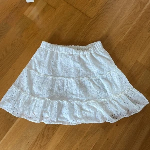 Vit kjol från Sister - Säljer en superfin vit kjol i storlek S. Kjolen har ett vackert broderat mönster och volanger som ger den en romantisk känsla. Perfekt för sommardagar eller en festlig tillställning. Den är i nyskick och har en elastisk midja för extra komfort. Passar perfekt till en enkel topp eller blus!, (nypris 350kr)
