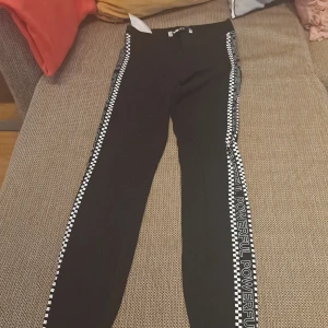 Svarta leggings med textdetalj från FB Sister - Säljer ett par svarta leggings från FB Sister i storlek XS. De har en cool textdetalj längs sidorna med ordet 'POWERFUL' och ett schackrutigt mönster. Perfekta för en avslappnad och sportig look!