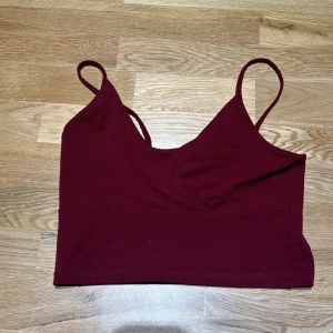 Vinröd croppad topp från FB Sister - Säljer en snygg vinröd croppad topp från FB Sister. Den är ärmlös med smala axelband och har en omlott-design framtill. Perfekt för sommarens fester eller en avslappnad dag ute. Toppen är i bra skick och superbekväm att bära!