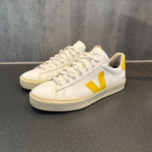 Vita sneakers från Veja med gula detaljer - Säljer ett par snygga vita sneakers från Veja med gula detaljer. Bra skick pris kan diskuteras!