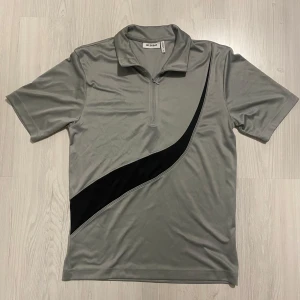 Grå kortärmad tröja från Weekday - Snygg grå kortärmad tröja från Weekday med en svart diagonal detalj framtill. Tröjan har en dragkedja vid halsen och är perfekt för en sportig look. Priset kan diskuteras!