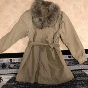 Jacka med päls - Snygg beige kappa med mjuk päls på kragen och insidan. Jackan har knappar och ett bälte i midjan . Äkta päls! Varm o mysig