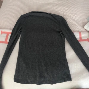 Mörkgrå långärmad topp  - Säljer en stilren mörkgrå långärmad topp från MNG. Perfekt för en enkel och elegant look. Toppen har en figurnära passform och är tillverkad i ett mjukt material.