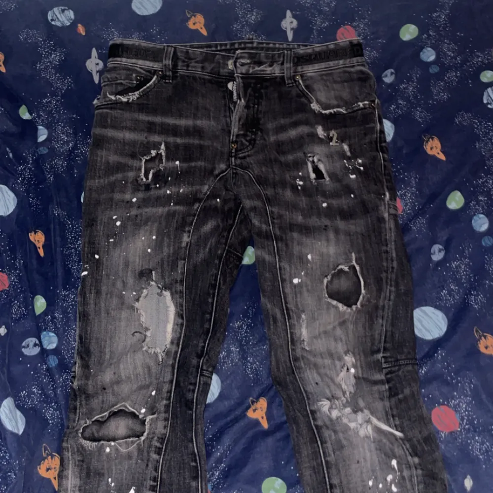 Säljer ett par svarta jeans från Dsquared2 i storlek 45. De har en cool, sliten look med flera hål och slitningar. Perfekta för en avslappnad och trendig stil. Passar bra till både vardag och fest!. Jeans & Byxor.