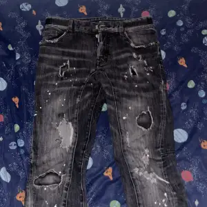 Säljer ett par svarta jeans från Dsquared2 i storlek 45. De har en cool, sliten look med flera hål och slitningar. Perfekta för en avslappnad och trendig stil. Passar bra till både vardag och fest!