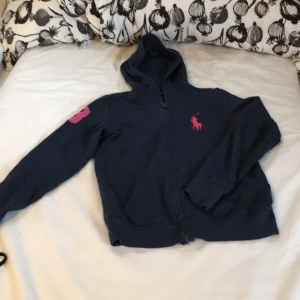 Mörkblå hoodie från Ralph Lauren - Säljer en snygg mörkblå hoodie från Ralph Lauren i storlek 12-14. Den har en dragkedja framtill och en stor rosa logga på bröstet. Perfekt för höst och vår, och den är i bra skick. Passar både till vardags och lite mer avslappnade tillfällen. 🧥💙